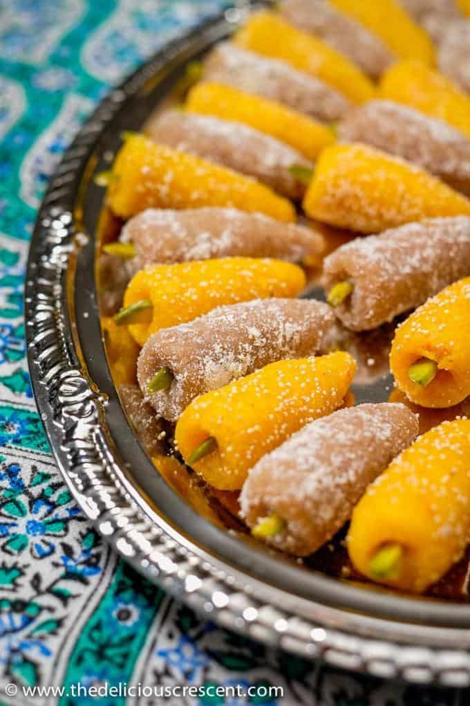 Persian marzipan candy (Toot) arranged on a plate placed on a blue floral table cloth.