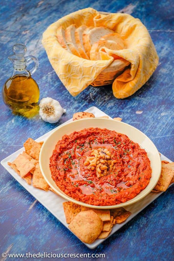 Muhammara served with pita chips and a basket of sliced bread.