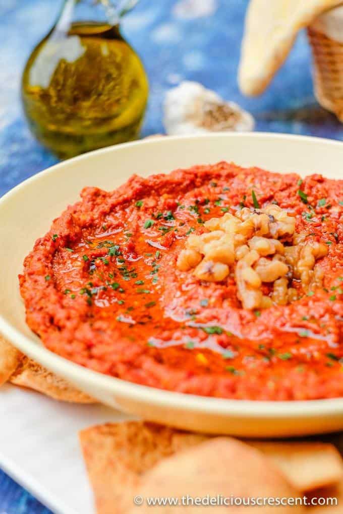 Muhammara served in a cream bowl with extra olive oil on the side.