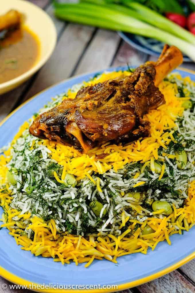 Baghali polo or Persian dill rice with lima beans is a fragrant rice recipe that pairs the pleasant flavors of dill, basmati rice and saffron with plump broad beans. All topped with a crunchy golden crust. This simple middle eastern rice is great with lamb shanks, chicken or fish and yogurt salad or cucumber salad for a weeknight dinner. It is gluten free, vegetarian and freezer friendly with tips to make it even more healthy. Vegan and lower carb options. #ricerecipes #Persianfood Baghali polo (Persial dill rice with lima beans) served with a lamb shank on a platter.