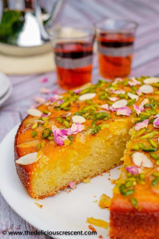 Persian love cake is moist, spongy and will enchant you with its exotic flavors of rose, cardamom, saffron. Luxuriously packed with almonds and sprinkled with pistachios, it is so easy to make! Great recipe for a traditional dessert to serve for holidays, wedding party or Valentines day. This Persian almond cake with cardamom and pistachios soaked in honey works well with rose water whipped cream. Gluten free and nut free options. #cake #dessert #Persianfood Close up view of Persian love cake after cutting a wedge.