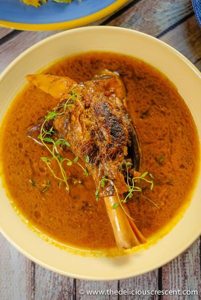 Braised lamb shanks slow cooked in an aromatic sauce with Persian spices, saffron, lemon juice and herbs makes a spectacular feast. The braising technique will give you succulent lamb with fall-off-the-bone tender meat in an amazingly delicious sauce! Let me show you how to cook lamb shanks in cast iron skillet or dutch oven with this easy middle eastern recipe. Including tips for cooking in oven or crockpot. #lambshanks #Persianfood Overhead view of lamb shanks with a fragrant Persian spiced sauce.