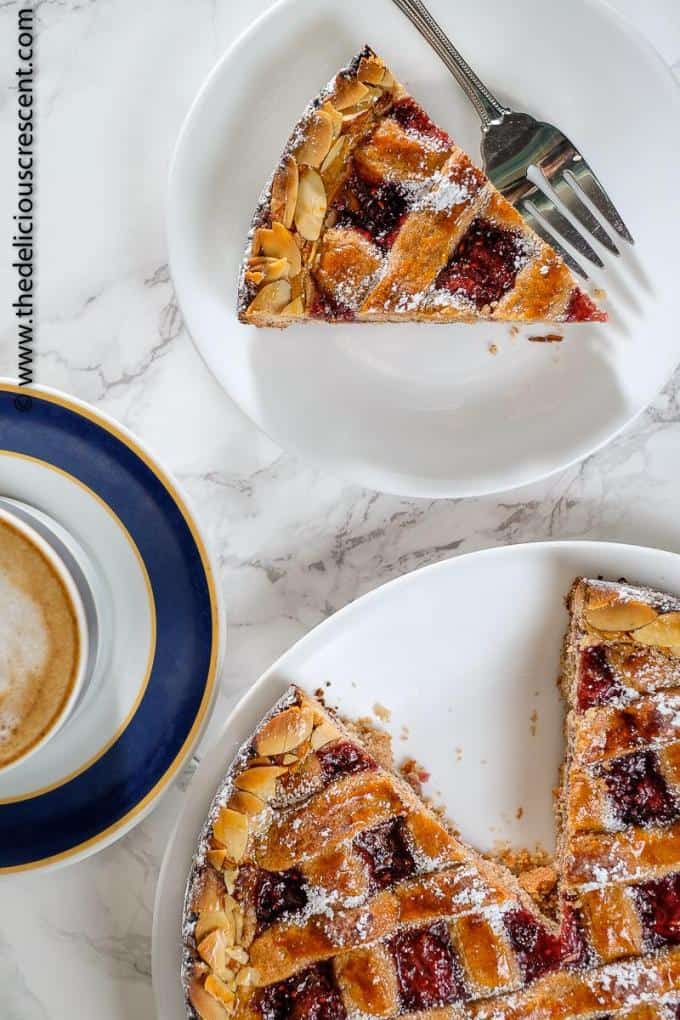 Linzer torte is a nutty, crumbly, rich pastry filled with jam and is as enchantingly pretty as it is tasty. It is easier than you would expect and delicious to the last bite! Perfect for entertaining. This dessert recipe is a specialty of Germany, Austria etc and is filled with raspberry jam and popular for holiday baking. Including suggestions for gluten free and dairy free options. #holidaybaking #torte #dessert. A slice of Linzer torte placed on a marble table.