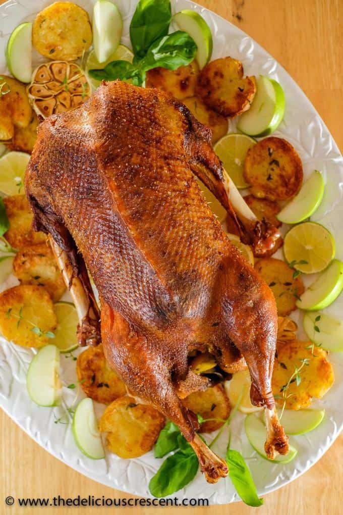 Whole roast goose placed on a serving platter with roasted potatoes