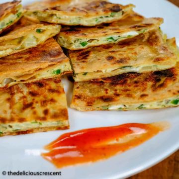 Egg paratha stuffed with omelette mixture, cut into pieces and served on a plate.