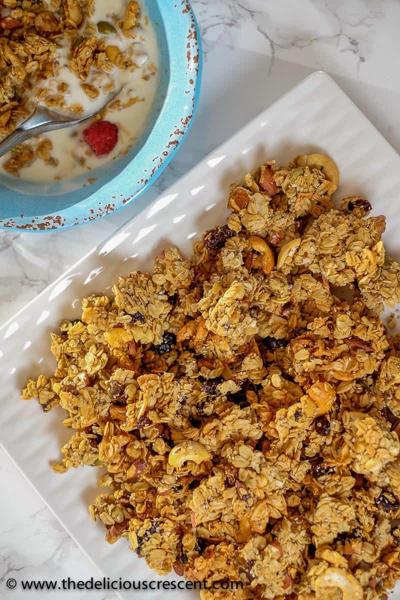 Overhead view of homemade granola on a white plate and also served with milk in a blue bowl.