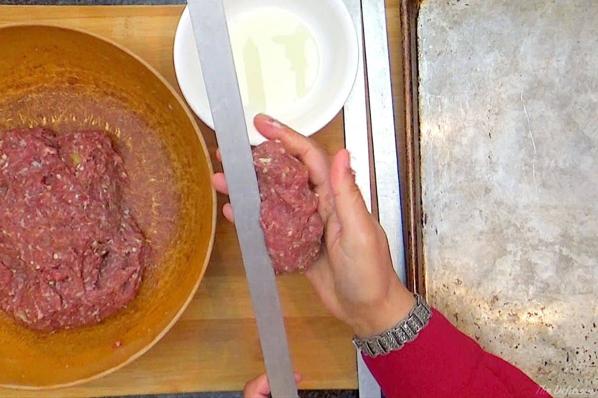 Shaping the meat mixture around metal skewers.