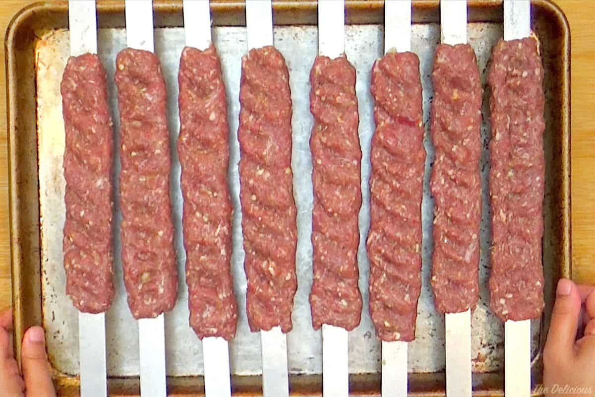 Ground meat skewers placed on a baking sheet.