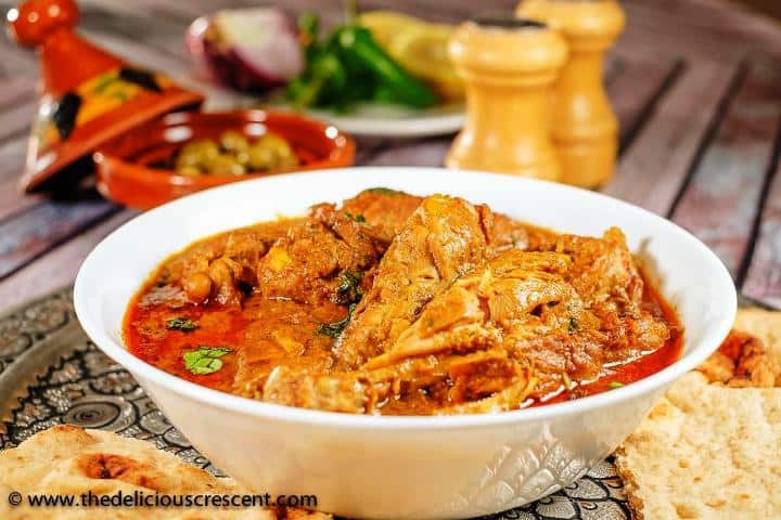 Chicken korma served on a table with naan, olives and some fresh vegetables.