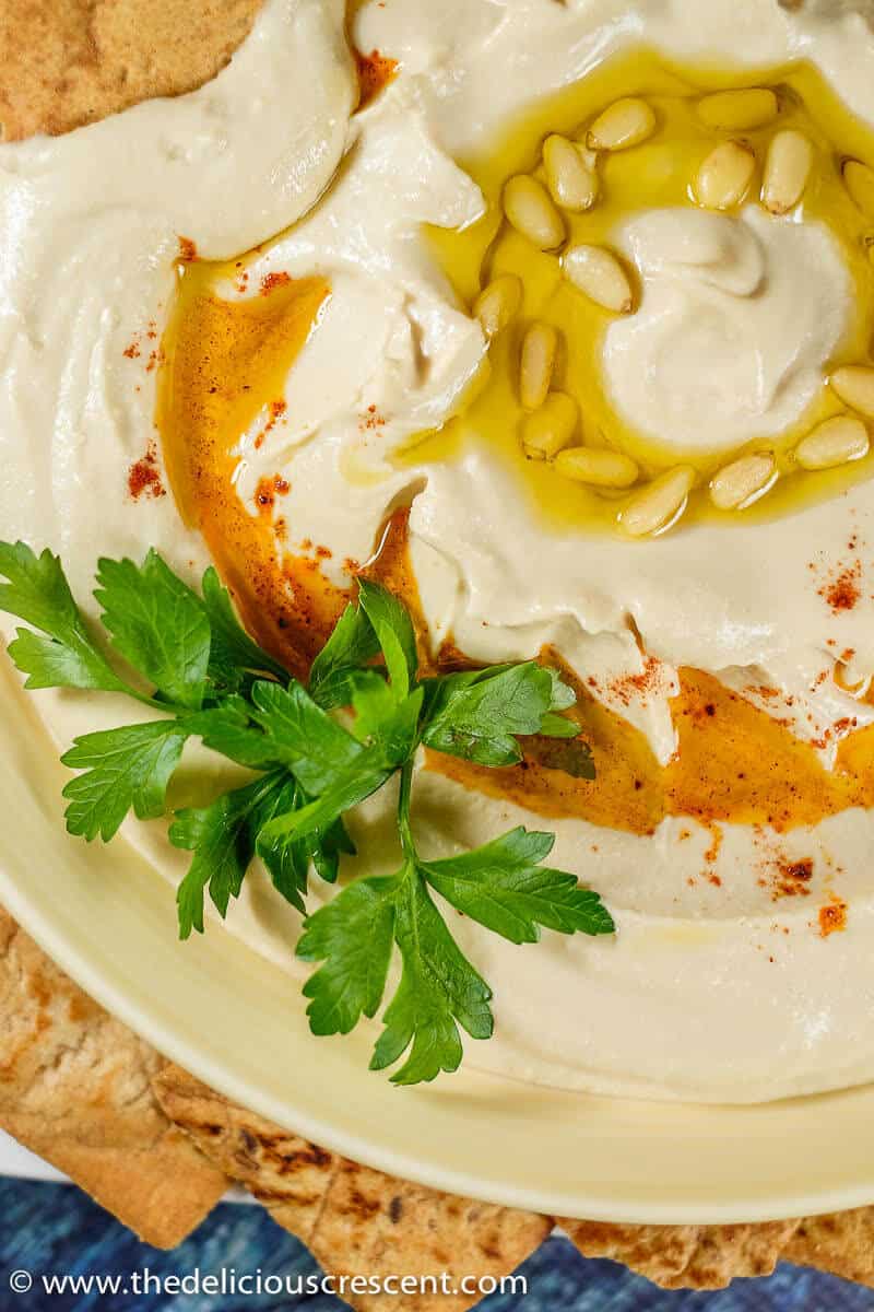 Close up view of ultra creamy hummus garnished with pine nuts, paprika and olive oil.
