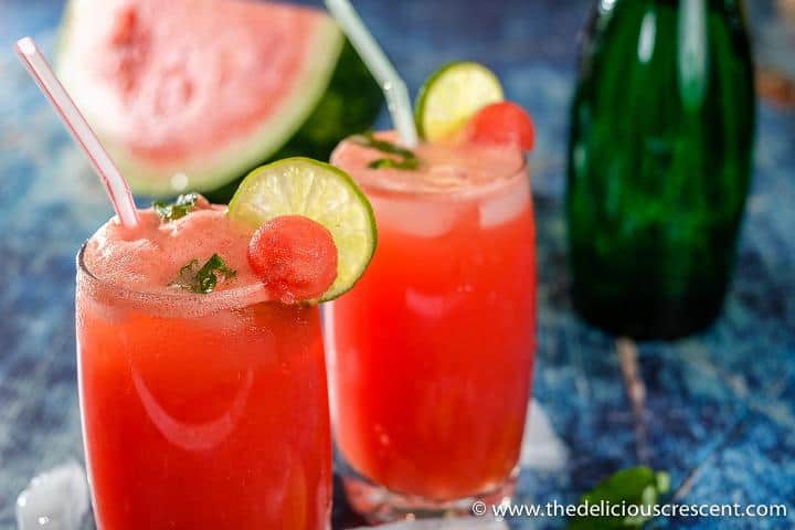 Two glasses of watermelon juice with the fruit in the background.