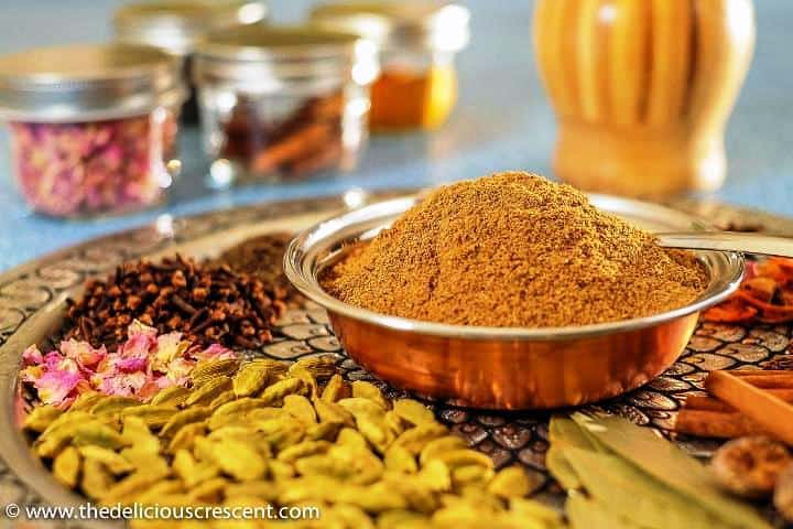 A bowl of ground garam masala with spices placed around it on a plate.