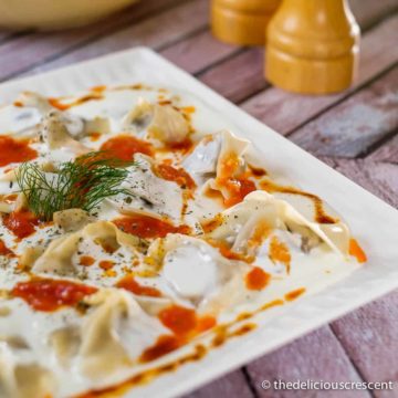 Vegetarian manti dumplings covered with yogurt sauce.