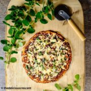 Cauliflower pizza served on a wooden cutting board.