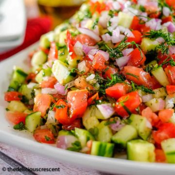 Persian tomato cucumber salad with fresh herbs served on a plate.