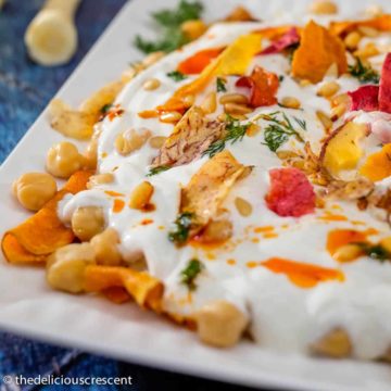 Chickpea salad with yogurt and vegetable chips served on a white plate.