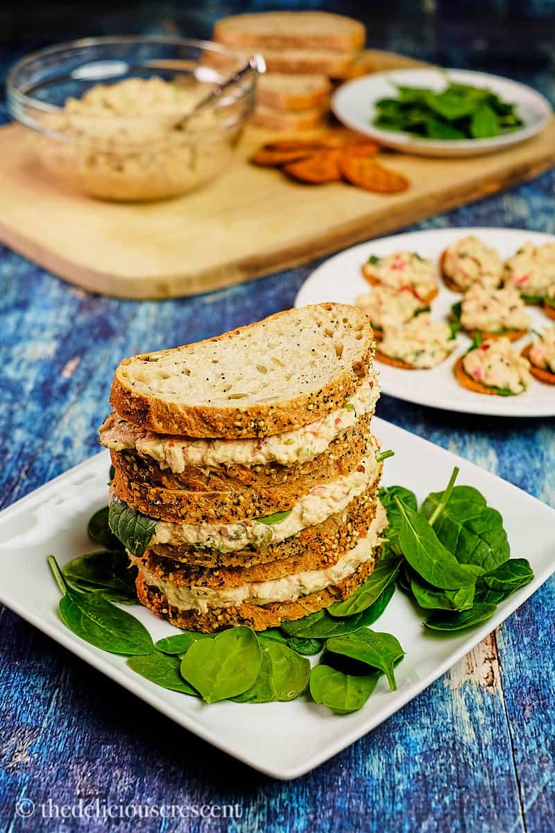 Spicy tuna salad sandwiches and crackers placed on a blue table.