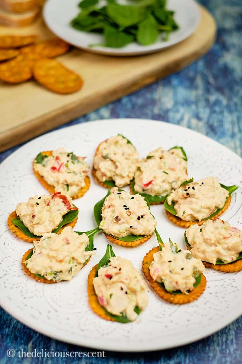 Tuna salad topped on crackers lined with spinach leaves.