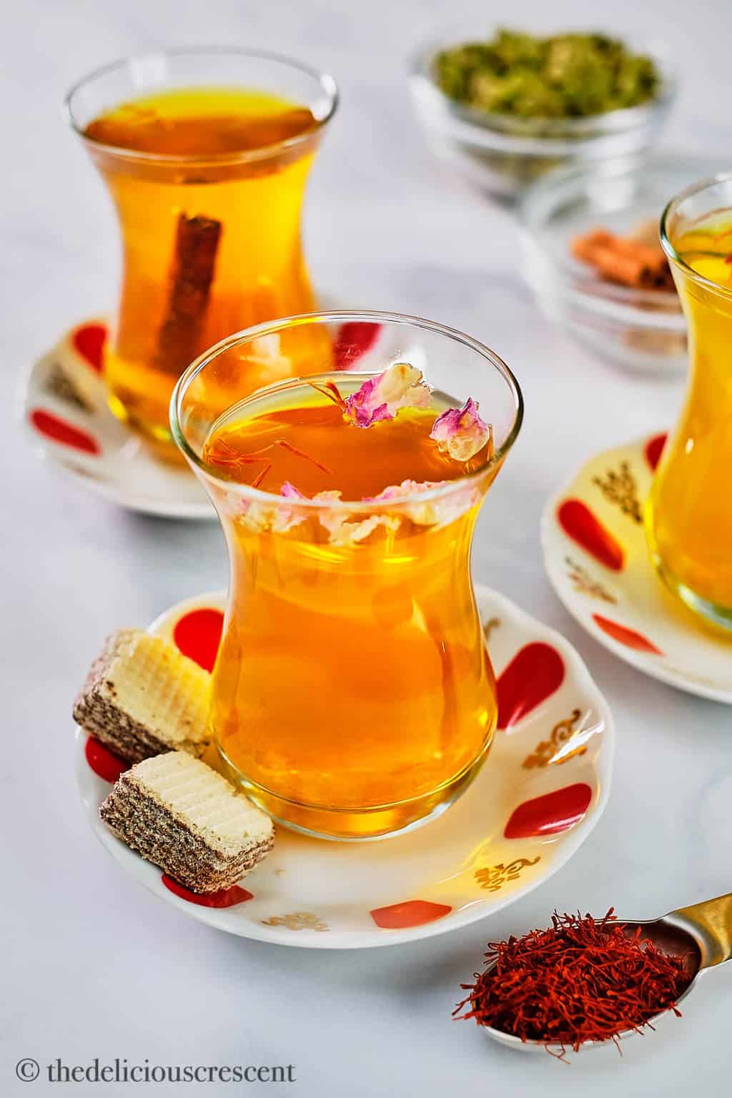 Saffron tea served in glass cups with rose petals, cinnamon and mint.