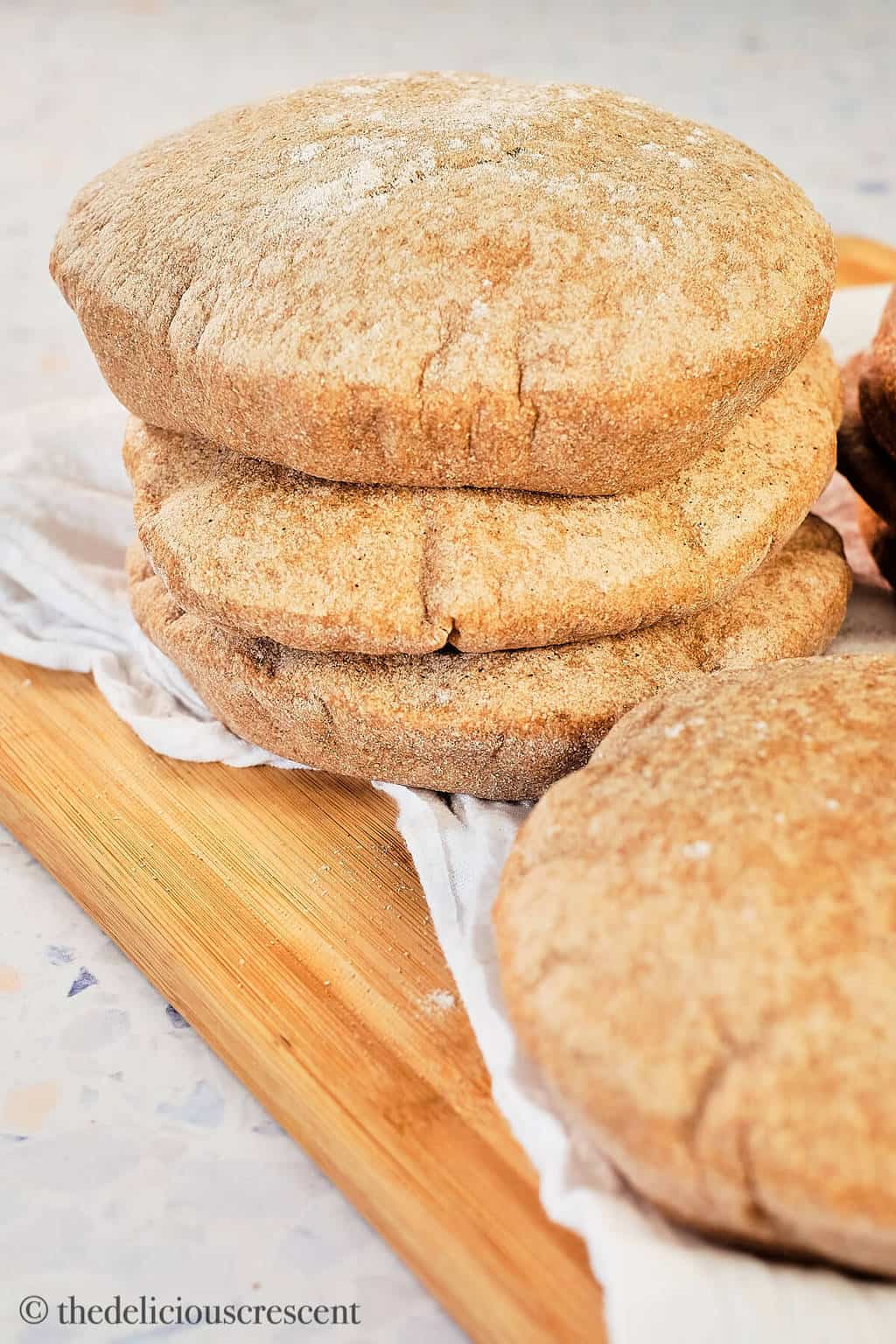 Puffed up whole wheat pita breads placed on a wooden board.