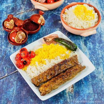 Kabab Tabei served on a white plate with rice and seared tomatoes and peppers.