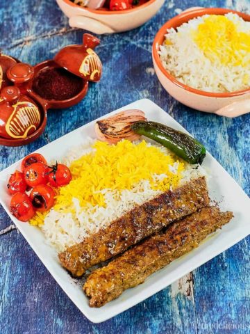 Kabab Tabei served on a white plate with rice and seared tomatoes and peppers.