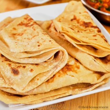 A stack soft parathas on a white plate.