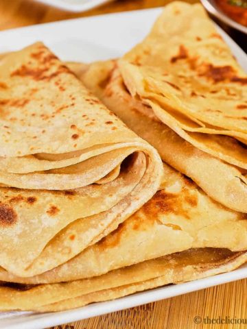A stack soft parathas on a white plate.