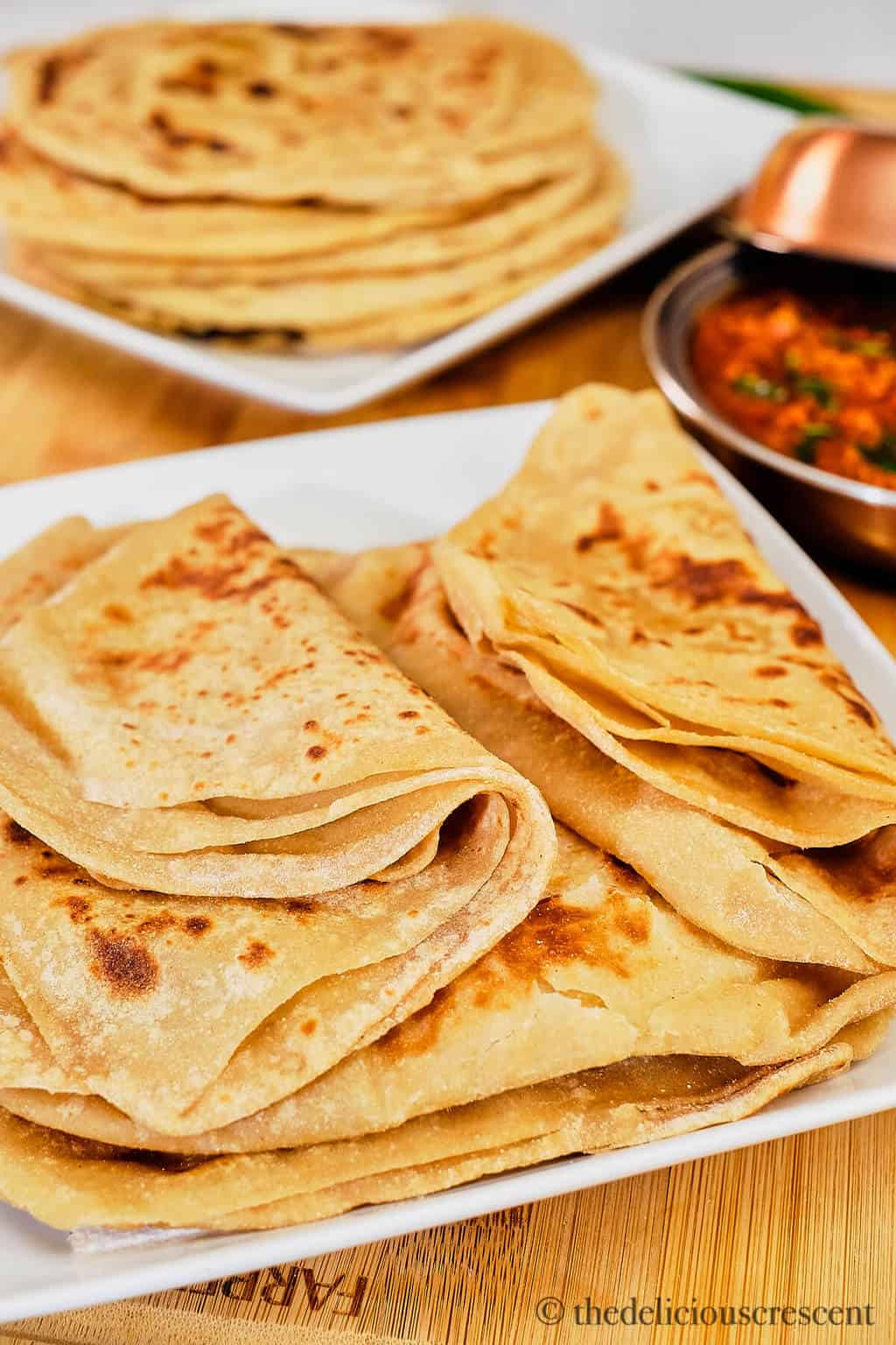 A stack soft parathas on a white plate.