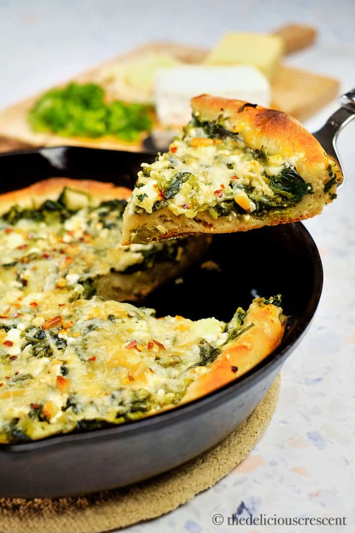 A wedge of spinach feta pizza lifted with a serving utensil.