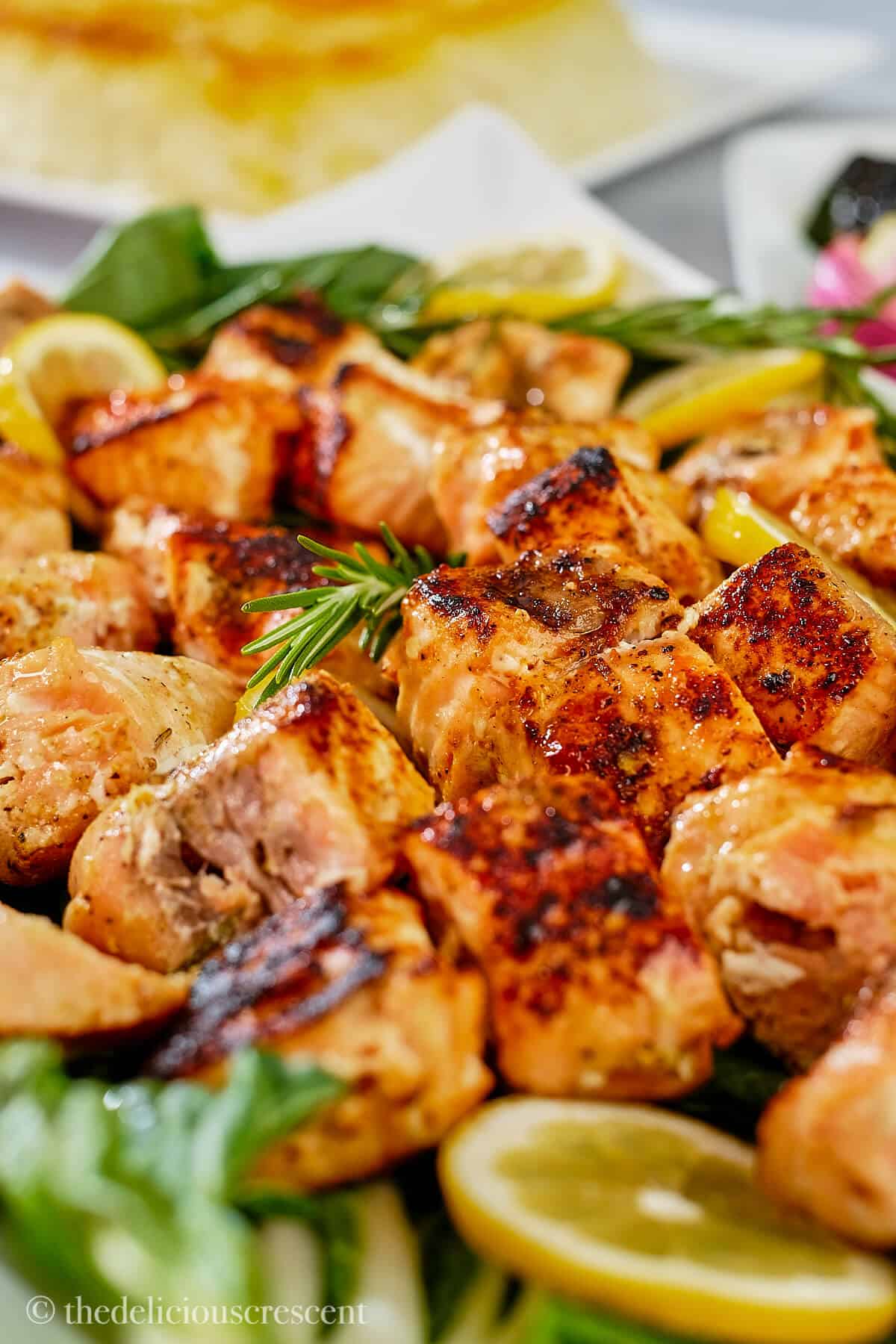 Salmon kebabs with lemon sliced placed on greens.