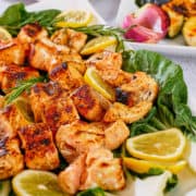 Grilled salmon kabobs and lemon slices arranged on a platter.