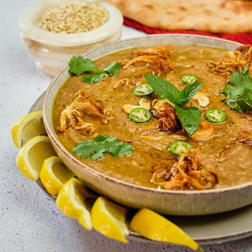 Haleem topped with fried onions, chili slices, herbs and lemon wedges.