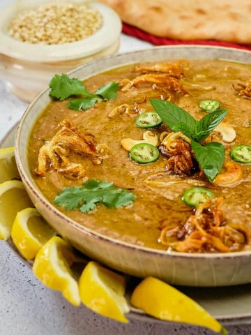 Haleem topped with fried onions, chili slices, herbs and lemon wedges.