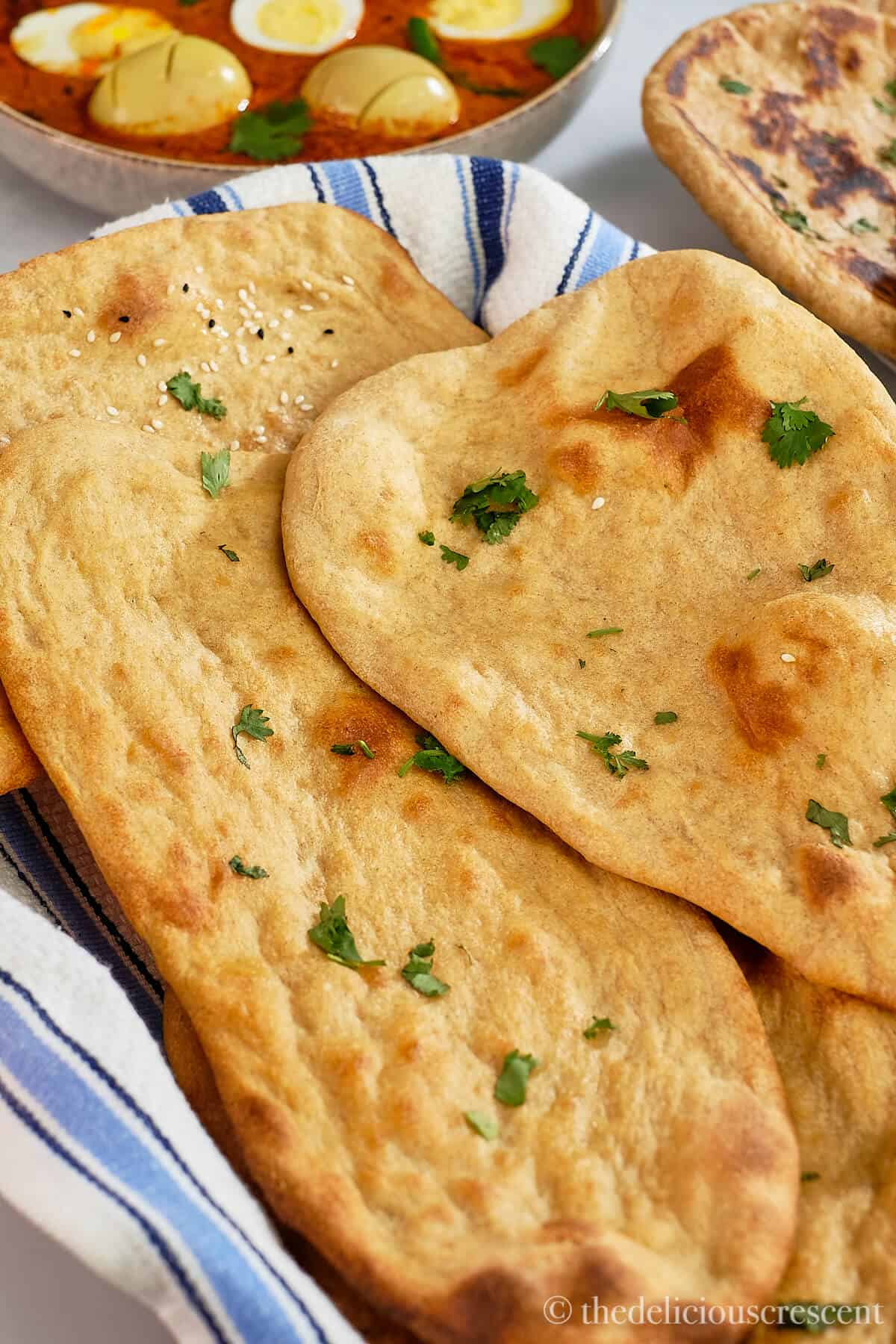 Two whole wheat naans on a kitchen towel.