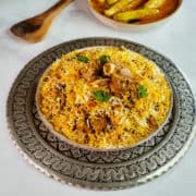 Close up view of a plate full of lamb biryani served with chili pepper curry.