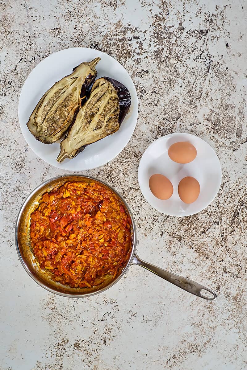 Roasted eggplants, eggs and stewed tomatoes on a table.