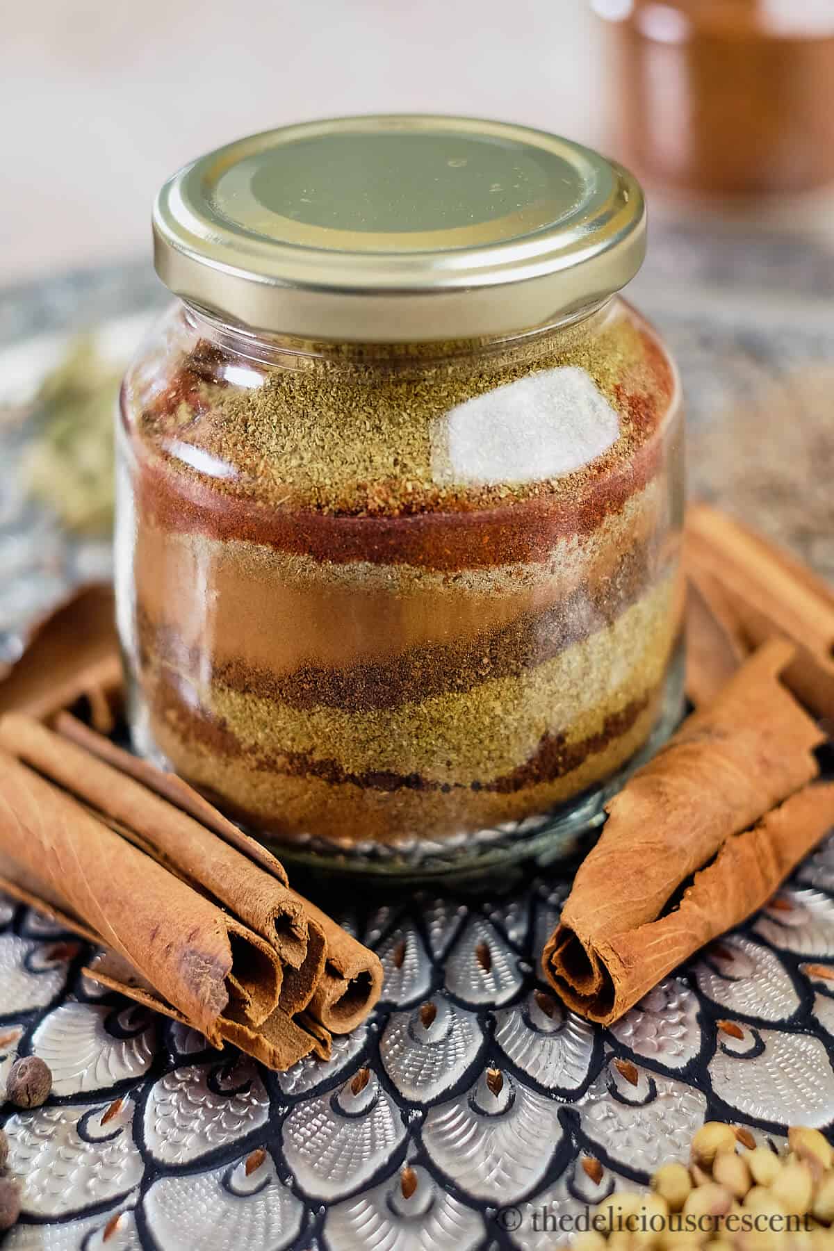 Layers of ground spices in a bottle surrounded by whole spices.