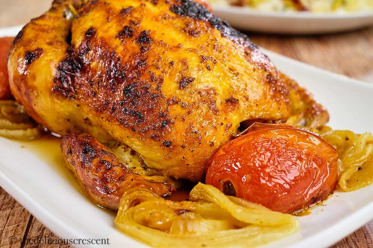 Roasted saffron chicken with tomato and onions on a plate.