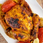 Close view of saffron chicken served with roasted vegetables on a white plate.