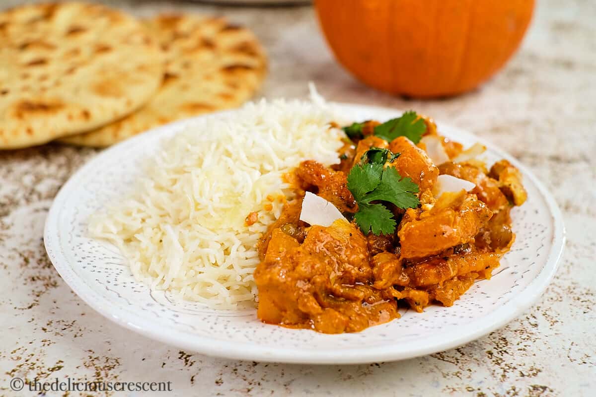 Pumpkin curry served with rice on a white plate.