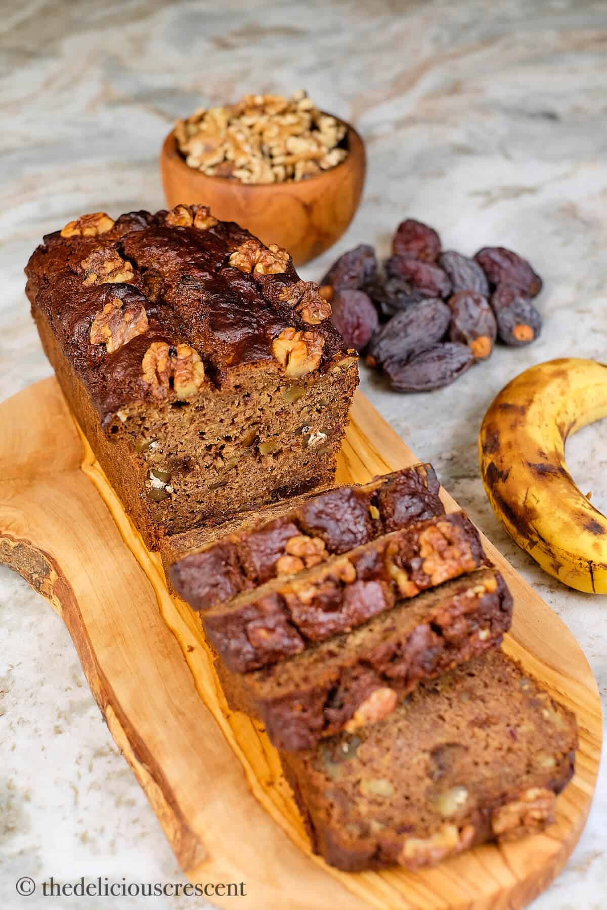 Date-sweetened banana bread with walnuts, sliced on a wooden board.