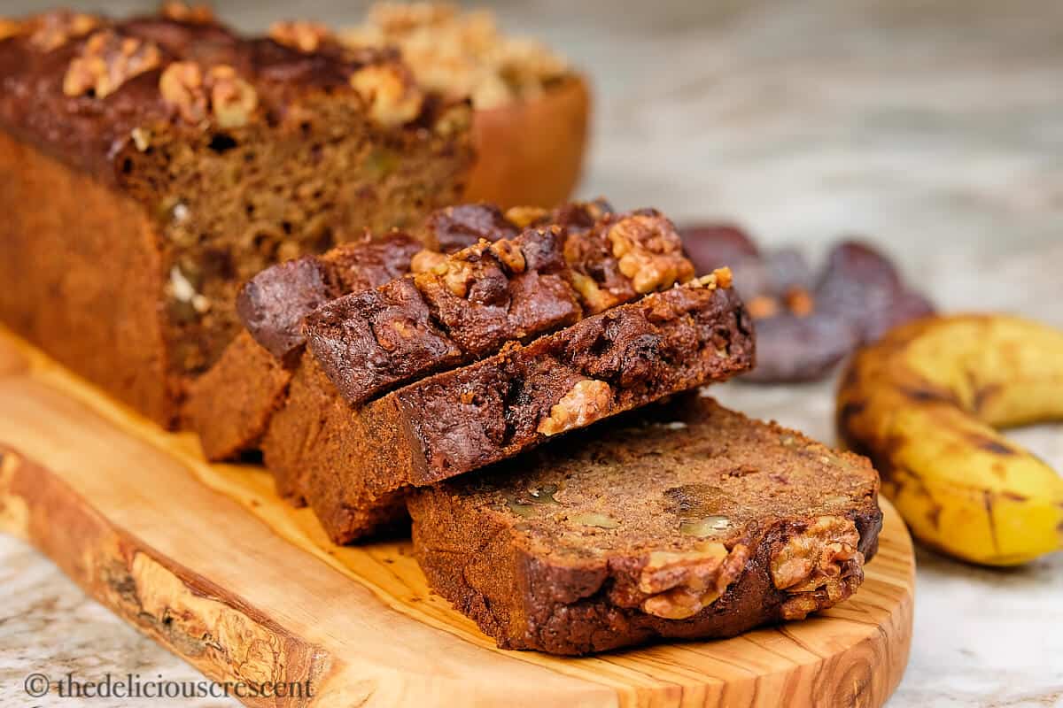 Date banana bread, sliced and served on a wooden board.